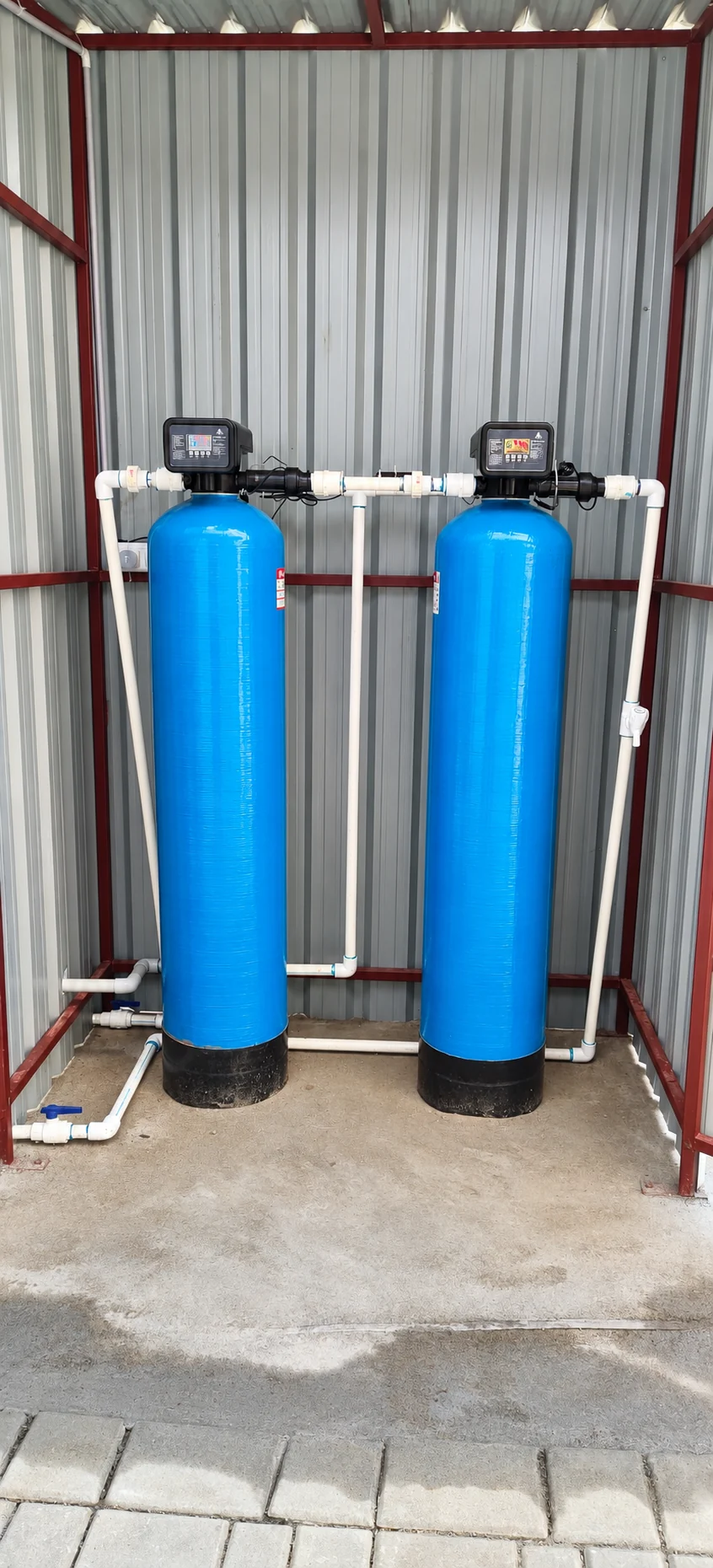 Two blue water filtration vessels with automatic control valves in a sheltered installation