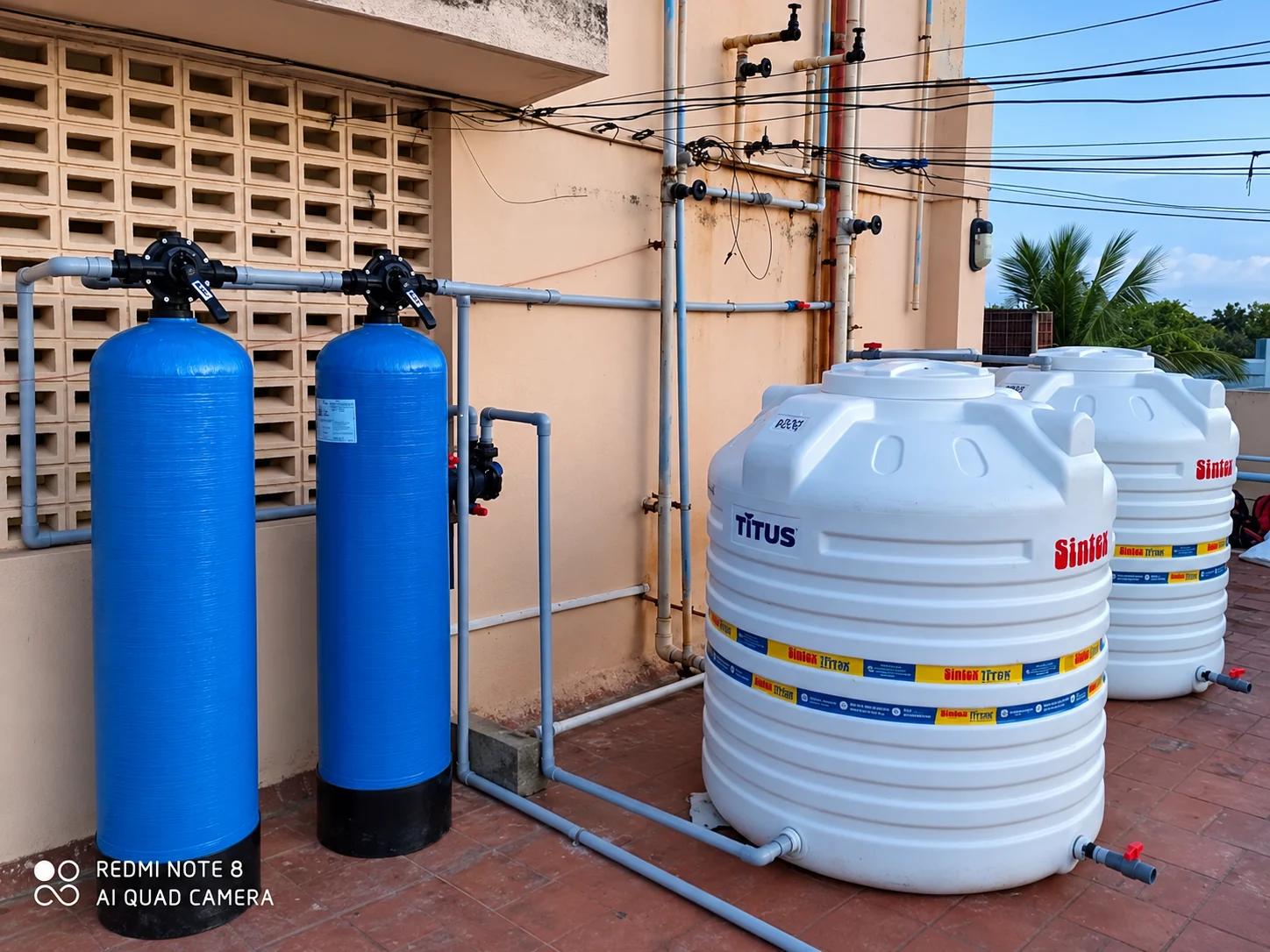 Rooftop installation with two blue filter vessels connected to white water storage tanks