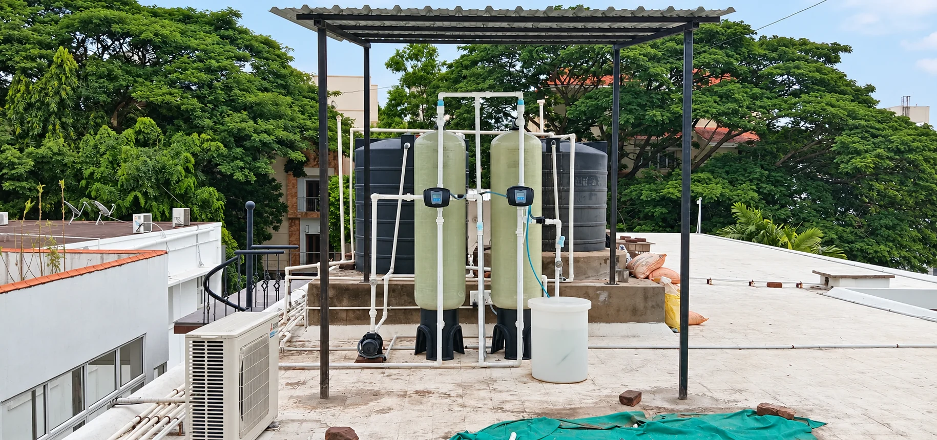 Rooftop filtration system beneath a metal canopy with twin vessels and black storage tanks