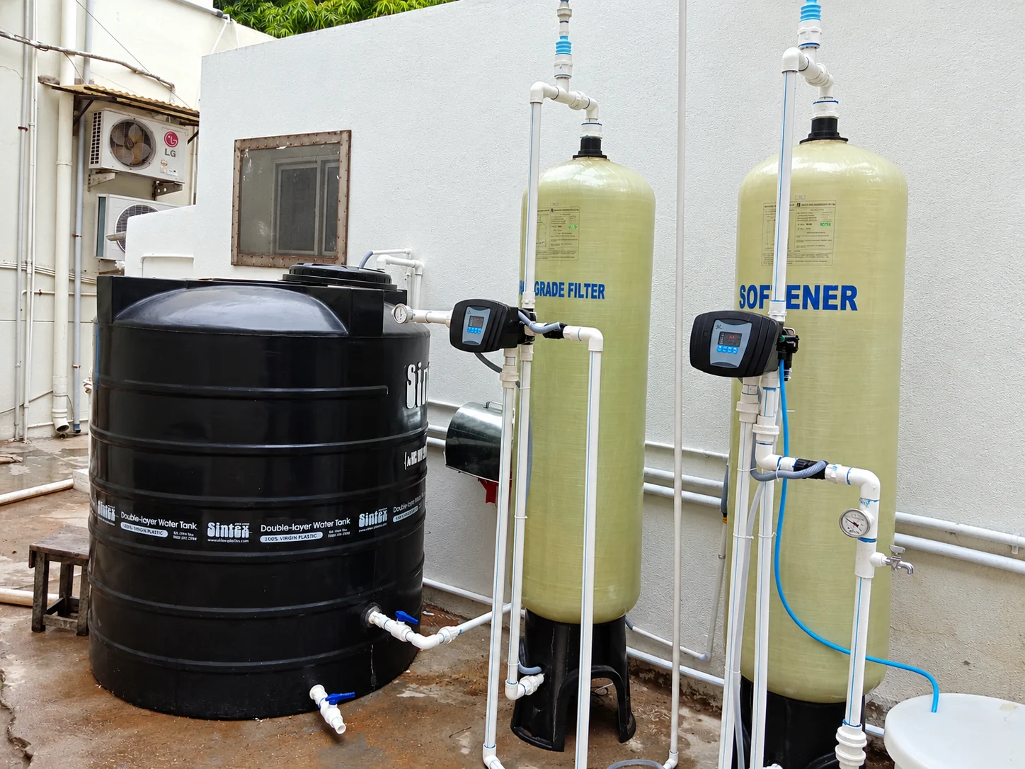 Outdoor multigrade filter and water softener with automatic controls beside a black storage tank