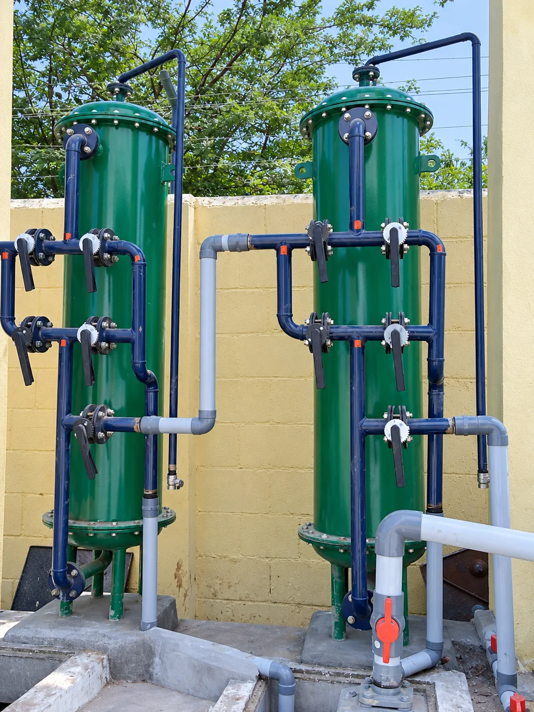 Two outdoor green pressure filter vessels with blue pipework and manual valves